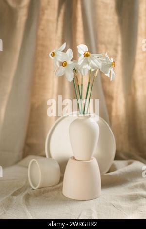 Bunch of white narcissus flowers in a vase with ceramic bowls on a table Stock Photo