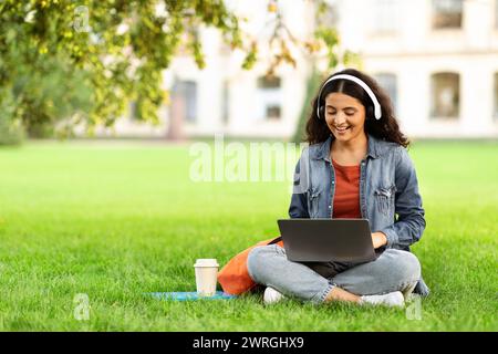Happy Eastern Woman Student Sitting On Lawn Outdoors With Laptop Stock Photo