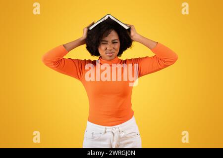 Frustrated young woman with a grimace, balancing a book on her head Stock Photo