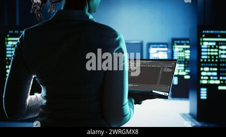 Meticulous expert working in server hub, running code on laptop, monitoring technologically advanced electronics clusters of blade servers, networking systems and storage arrays Stock Photo