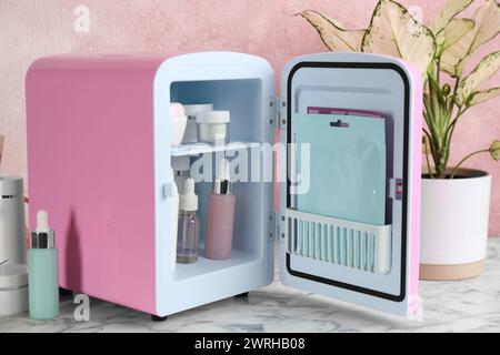 Open cosmetic refrigerator and skin care products on white marble table Stock Photo