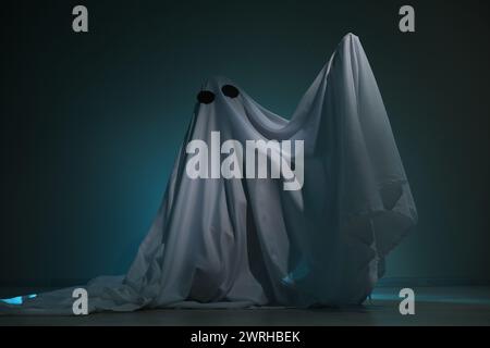Creepy ghost. Woman covered with sheet on dark teal background Stock Photo