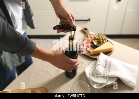 Man opening wine bottle with corkscrew at table indoors, closeup Stock Photo