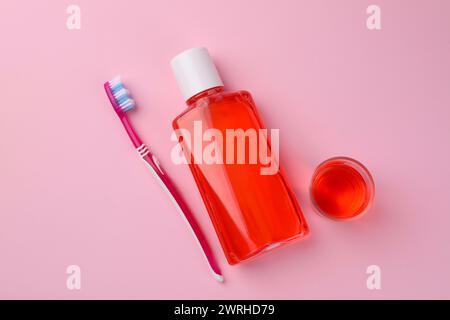 Fresh mouthwash in bottle, glass and toothbrush on pink background, flat lay Stock Photo