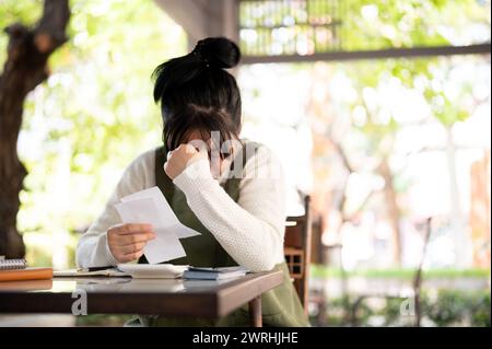 A stressed young Asian female small business owner is calculating bills, worried about her shop expenses and revenue, experiencing a financial crisis, Stock Photo