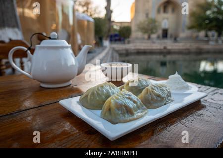 national dish of manti, khinkali, pelmeni, Pirogi, or dumplings with liver served with sour cream and bread sprinkled with sesame seeds. on the table Stock Photo