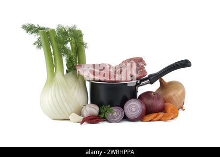 Black saucepan with pieces of raw pork inside. Around the saucepan are sliced vegetables which include onions, carrots, and garlic isolated on white b Stock Photo