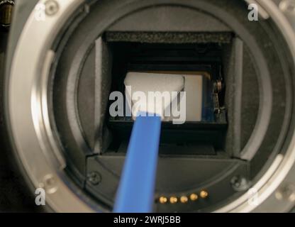 Technician cleans sensor of digital camera from dust and dirt using cleansing swab Stock Photo