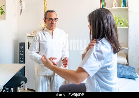 Qi gong therapist communicating with patient explaining her pain sitting on stretcher in a clinic Stock Photo