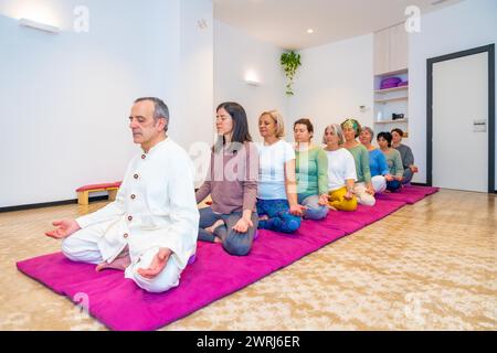 Yoga instructor and women meditating on a mat sitting in line in lotus position Stock Photo