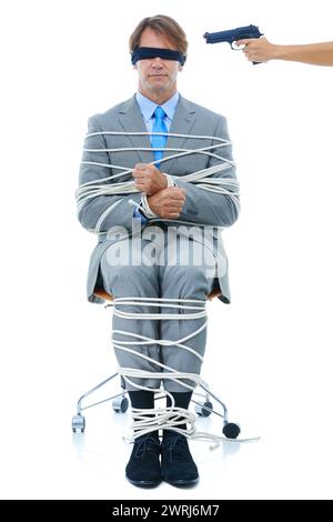 Businessman, tied up and hostage with gun on chair in kidnapped, robbery or silence on a white studio background. Young man or employee with ropes or Stock Photo