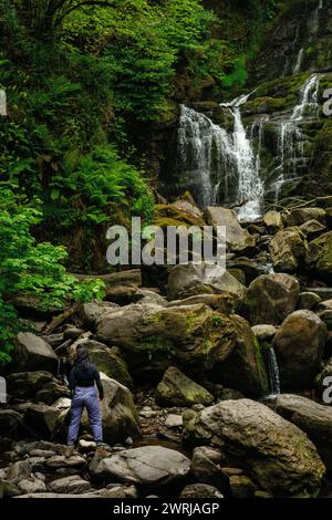 Young woman female hiker standing on boulders at Torc Waterfall in Killarney National Park, County Kerry, Ireland Stock Photo