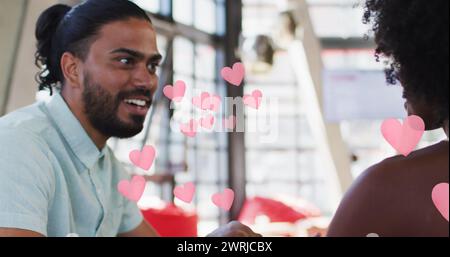 Pink heart icons against african american couple holding hands while sitting in a restaurant Stock Photo