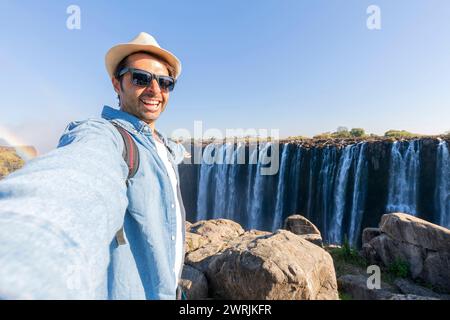 Tourist with a backpack at the Victoria Falls on Zambezi River located at the border of Zambia and Zimbabwe, the largest waterfall in the world. Stock Photo