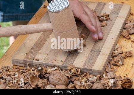 Man cracking walnuts with hammer at table, closeup Stock Photo