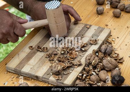 Man cracking walnuts with hammer at table, closeup Stock Photo