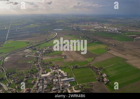 In this aerial view of a rural area in the Pianura Padana, lush green fields dominate the landscape. Farms and small settlements can be seen scattered Stock Photo
