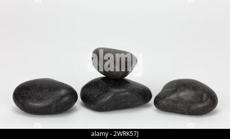 Four dark polished pebbles or rocks, one centre balanced, against a pale background with copy space Stock Photo