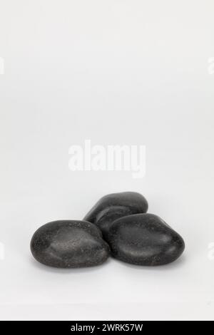 three black pebbles against a pale editable background shot in high resolution and editable portrait format can be used in composite, with copy space Stock Photo