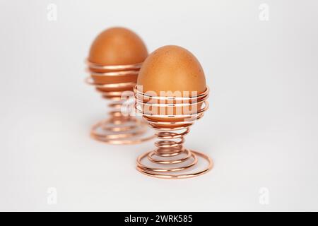 two large free range eggs in rose gold or copper spiral egg cups against a pale background editable Stock Photo