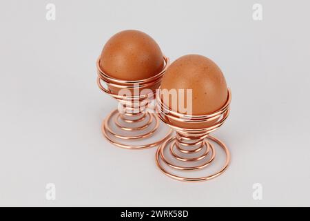 two large free range eggs in rose gold or copper spiral egg cups against a pale background editable Stock Photo