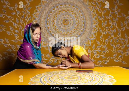 Indian artisan is applying mehndi on the hands of a white skin bride wearing a saree.  Stock Photo