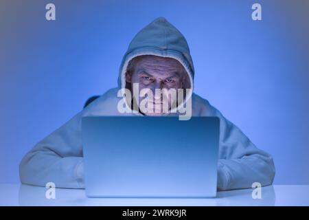 Older criminal man using computer for remote money robbery Stock Photo