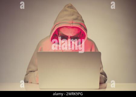 Older criminal man using computer for remote money robbery Stock Photo