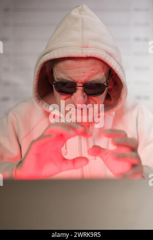 Older criminal man using computer for remote money robbery Stock Photo