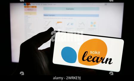 Person holding smartphone with logo of software machine learning library scikit-learn in front of website. Focus on phone display. Stock Photo