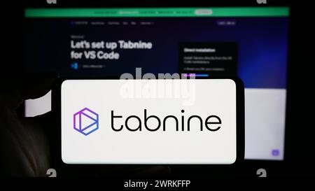 Person holding cellphone with logo of Israeli AI coding company Tabnine Ltd. in front of business webpage. Focus on phone display. Stock Photo