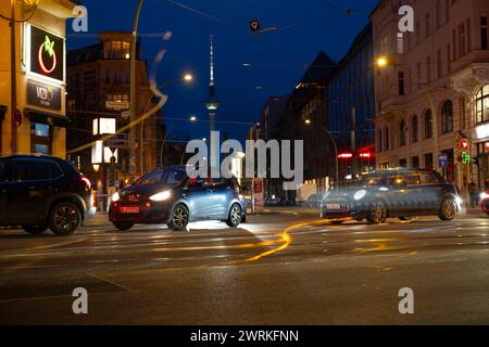 Cars driving down night Oranienburger street, Illuminated buildings and Fernsehturm TV tower visible in background, Nightlife, sustainability and envi Stock Photo