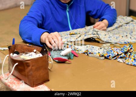 The picture shows a seamstress who has laid out the fabric on the table and is doing something with it. Stock Photo