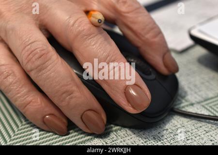 In the close-up picture, a woman's hand, between the fingers of which a pencil is visible, lies on a computer mouse. Stock Photo