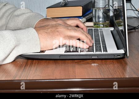 Side view of a man, his hands, which is typing text on a laptop. Stock Photo