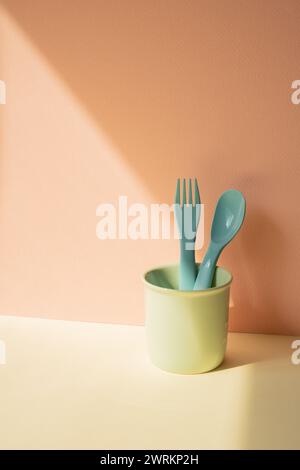 Kitchen blue cutlery fork and spoon in holder on ivory table. pink wall background Stock Photo