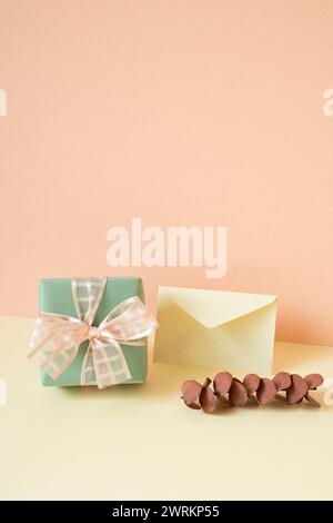 Green gift box, envelope, eucalyptus leaf on ivory table. pink wall background Stock Photo