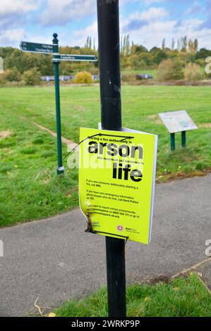 Police sign on a park lamp post warning public of serious penalties for arson.  The sign has been vandalised with a flame and is melted and warped. UK Stock Photo