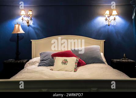 A bed with a white headboard and pillows, and a lamp on the nightstand. The room is decorated in blue and white, giving it a calm and serene atmospher Stock Photo