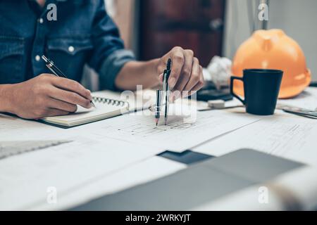 Architect using divider compass working on blueprint and make a note on book. Construction concept. Engineering tools Stock Photo