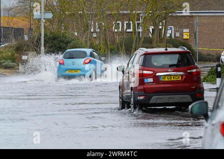 Weymouth, Dorset, UK.  13th March 2024. UK Weather:  Cars drive through floodwater from a high spring tide on Commercial Road next to the harbour at Weymouth in Dorset on a warm overcast morning.  Picture Credit: Graham Hunt/Alamy Live News Stock Photo