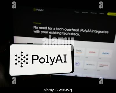 Person holding smartphone with logo of conversational artificial intelligence company PolyAI Ltd. in front of website. Focus on phone display. Stock Photo