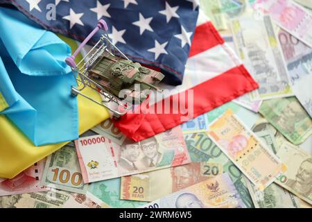 Toy tank on US flag and ukrainian flag on many banknotes of different currency. Background of war funding and military support between United States and Ukraine Stock Photo