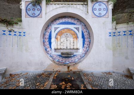 Fonte dos Pisões fountain with drinking water in Sintra, Portugal. Fountain from 1931 with tiled panel and stone relief of children holding cups and p Stock Photo