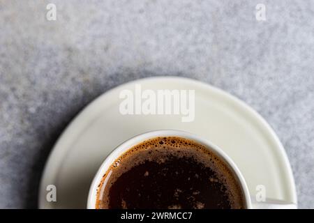 A top view of a freshly brewed hot coffee in a white cup placed on a saucer, with a foamy surface, perfect for a morning energy boost. Stock Photo