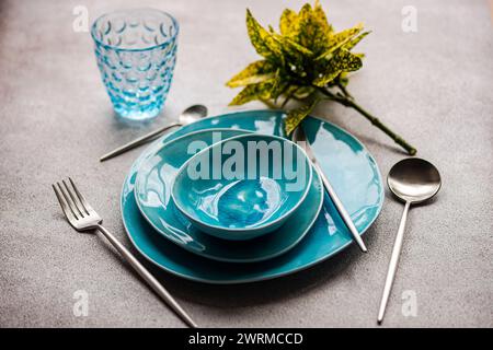 Vibrant teal dinnerware set with matching glass and cutlery on a textured grey surface. Stock Photo