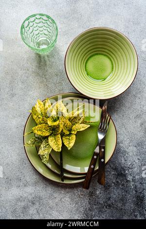 Top view of a sophisticated table setting featuring bright green ceramic dishes, complemented by sleek cutlery and a decorative glass on a textured su Stock Photo