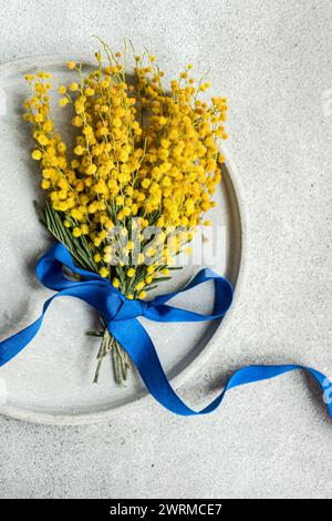 From above of charming mimosa flower sprig bound with a vivid blue ribbon, laid upon a textured table surface, creating a refreshing visual contrast Stock Photo
