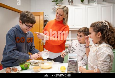 A joyful family moment as a mother guides her children in baking activities in a cozy home kitchen, reinforcing the concept of Family Gathering. Stock Photo