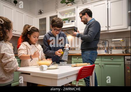 A heartwarming family scene as kids and an adult engage in cooking activities in a homey kitchen, adding to the warmth and joy of a family gathering. Stock Photo